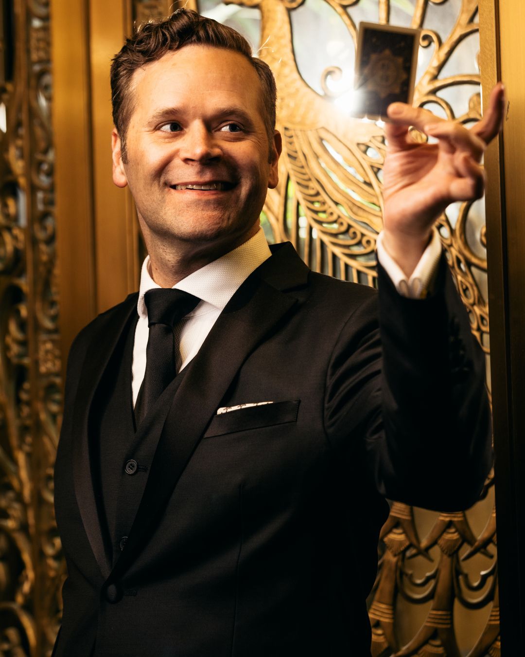 Dennis Watkins holding a card in front of a gold background.