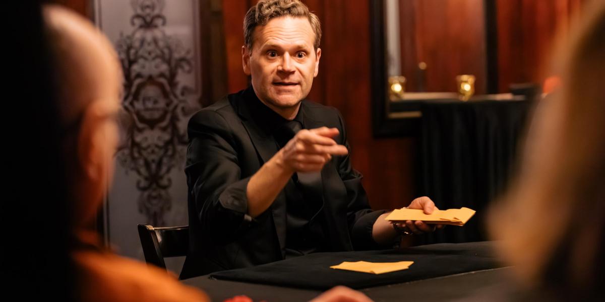 Dennis Watkins sitting at a table performing magic for a small group of guests.