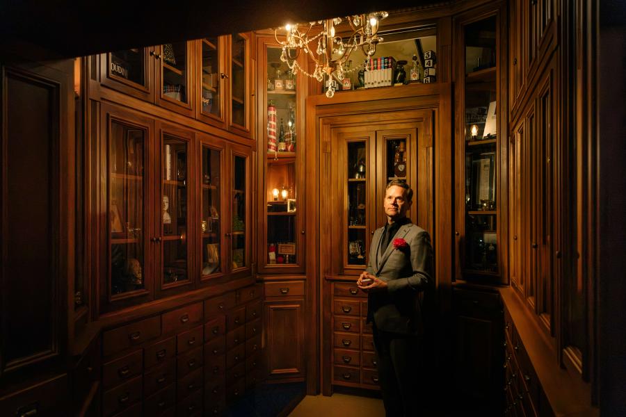 Dennis standing surrounded by wooden cabinets filled with magic props.